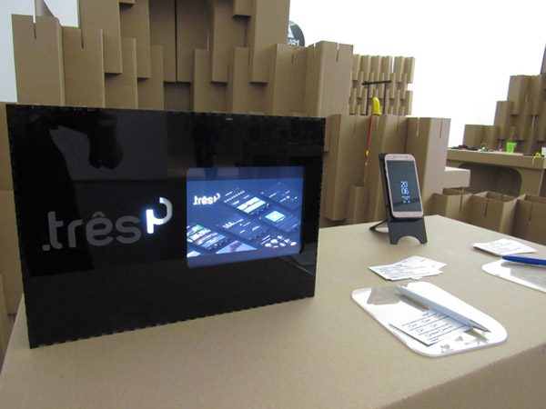 Exposição em uma mesa de uma tela em acrílico com tablet e um celular mostrando o projeto